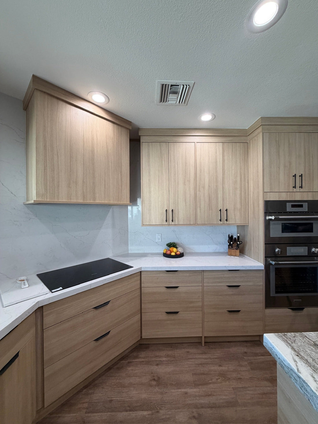 European-style kitchen remodel in Mesa AZ with light wood custom cabinets, quartz countertops and backsplash, and built-in double ovens