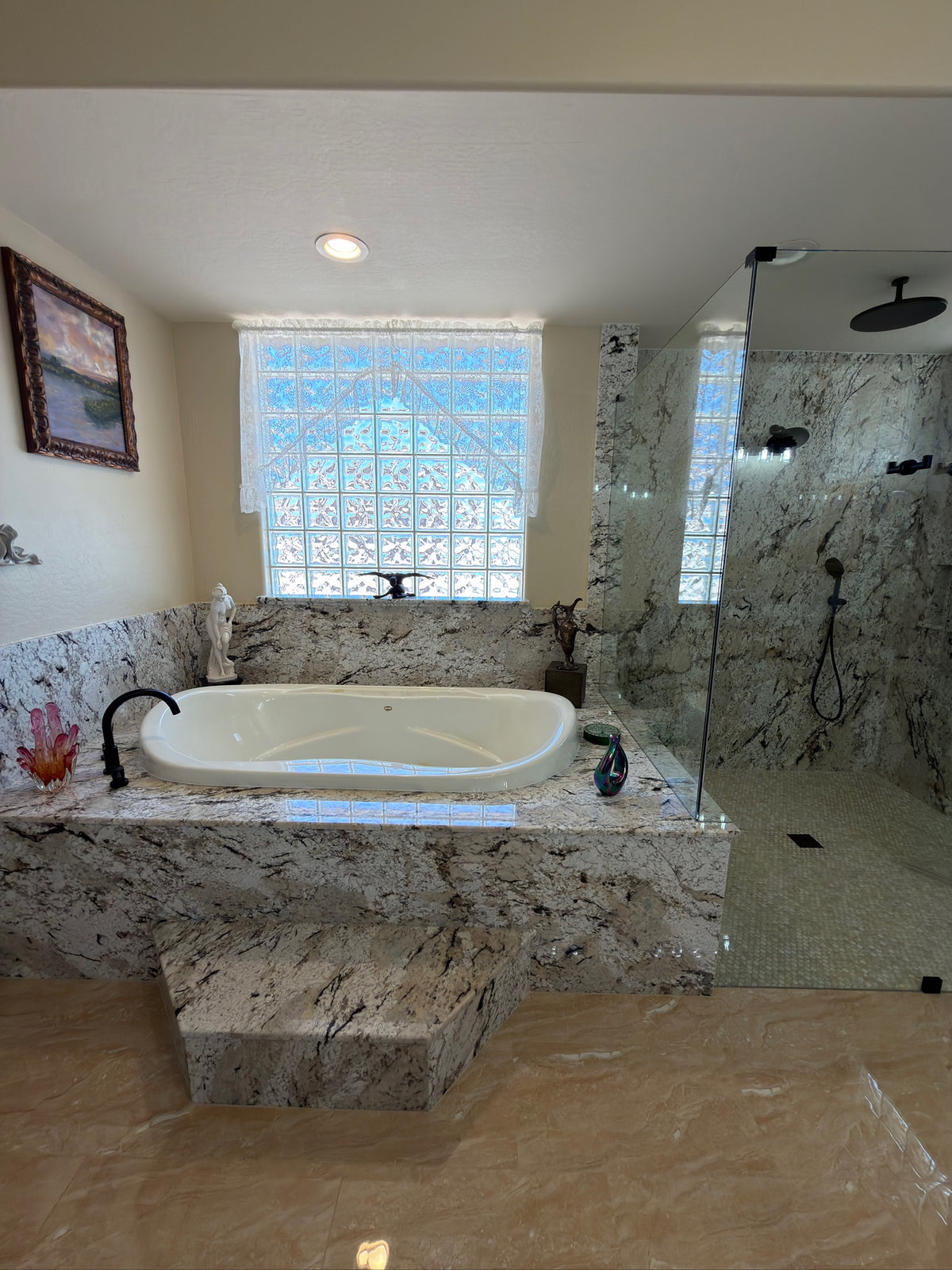 A luxury bathroom featuring a raised white jacuzzi tub set into a marble-tile platform, with a matching marble walkway and a glass-enclosed shower stall.