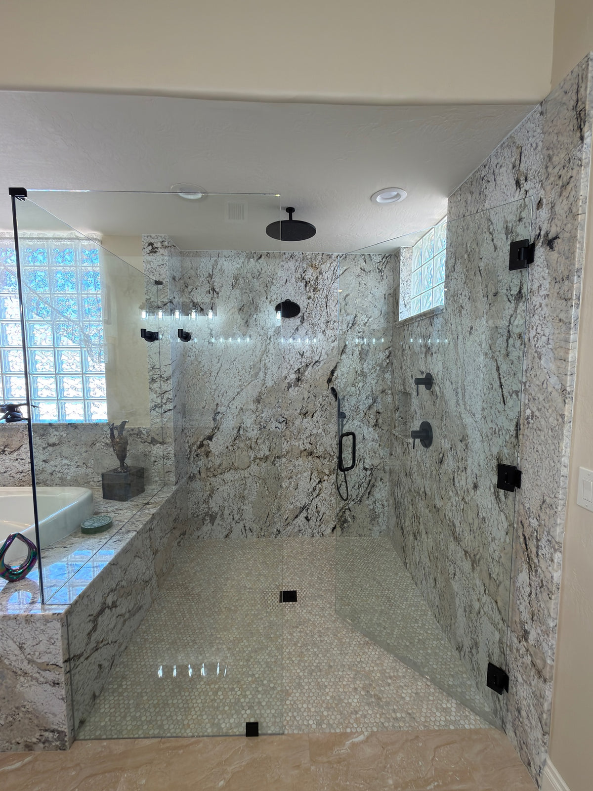 A modern walk-in shower stall with natural stone walls and tile floor, a glass door with a black frame, and black shower fixtures.